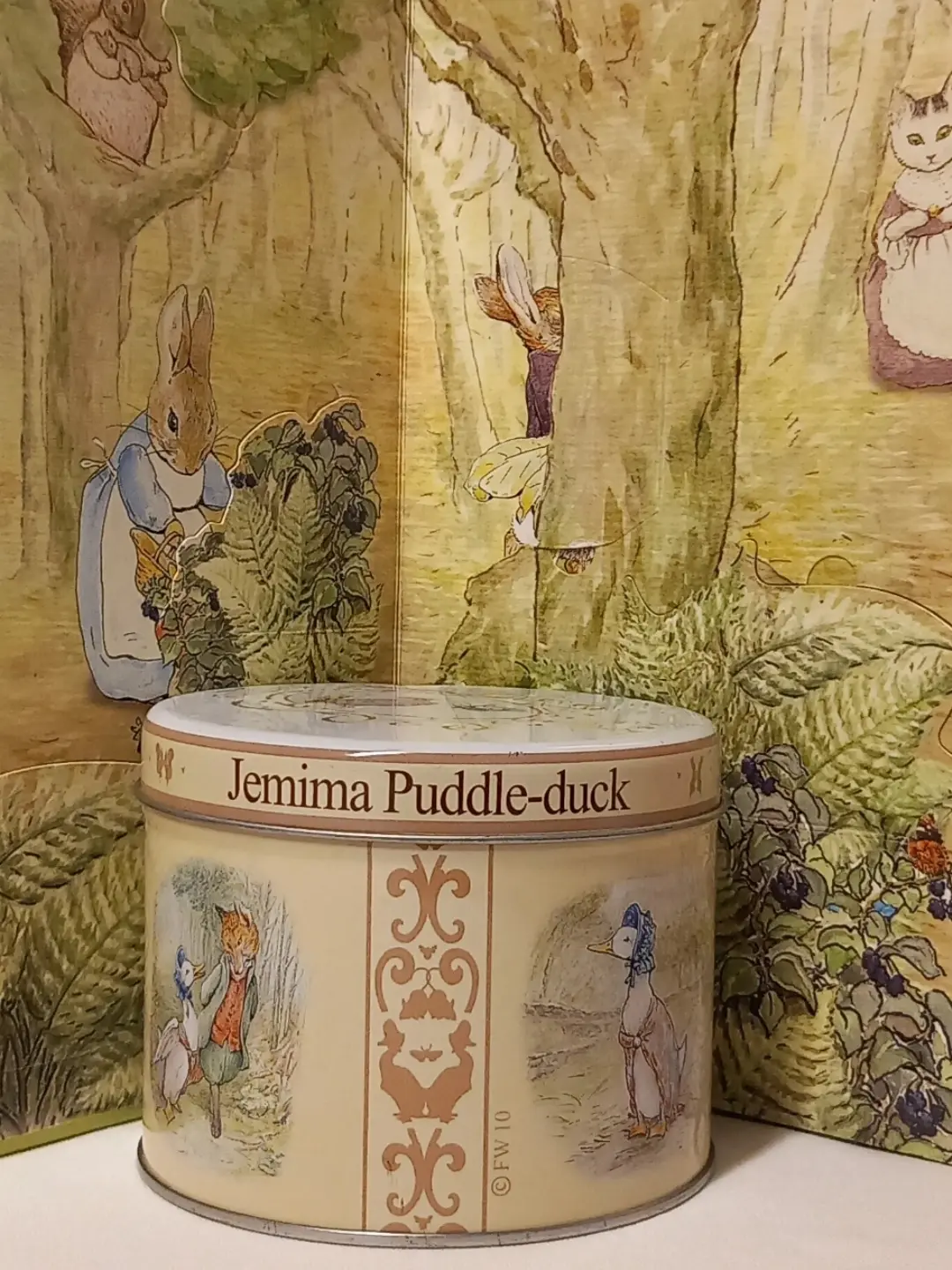 Teneke kutunun gövdesinde tilki ile Jemima ve boneli ördek çizimleri arasında süslü şerit