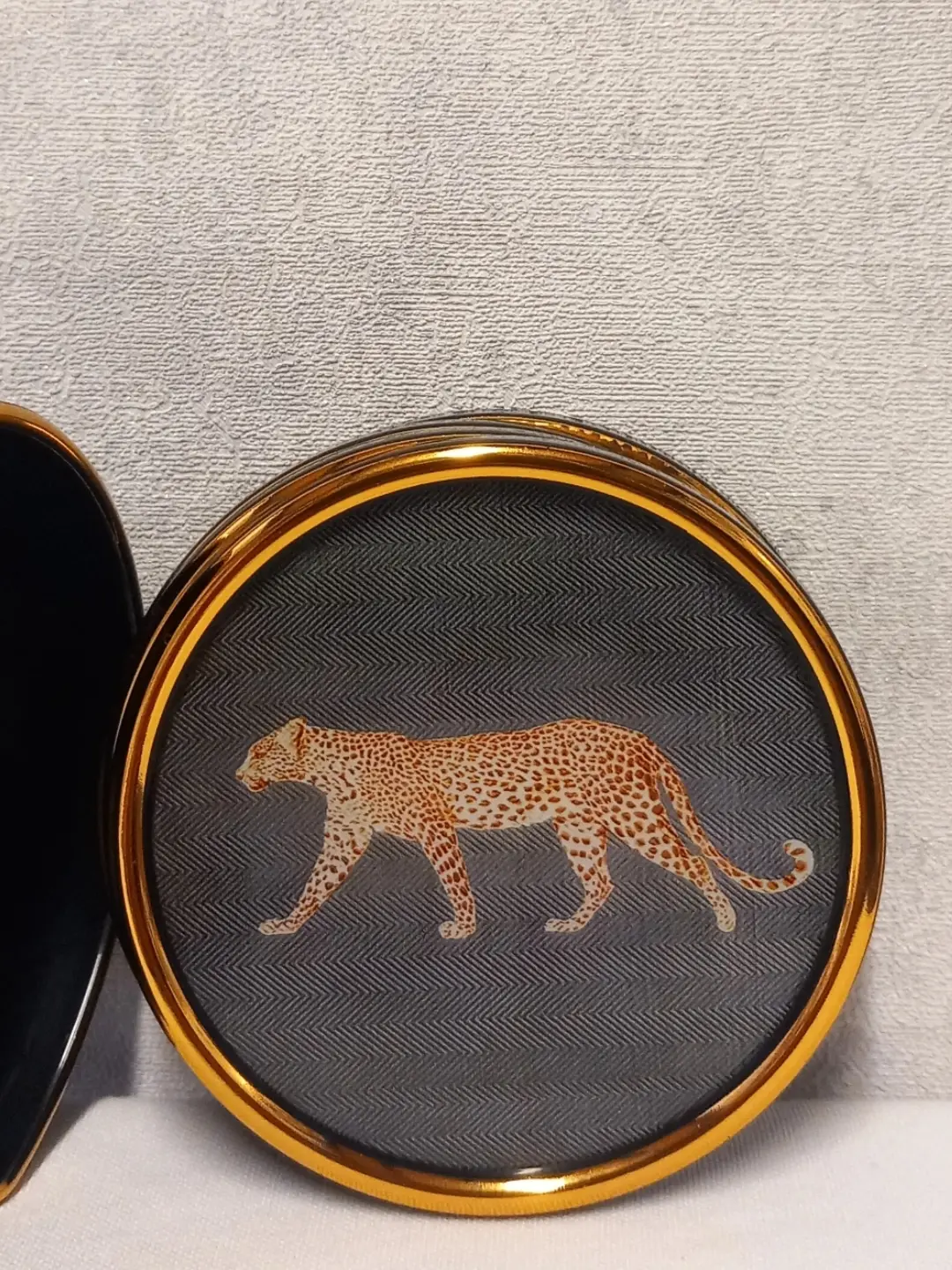 Herringbone dokulu gri zemin üzerinde yürüyen leopar desenli bardak altlığının yakın görünümü; solda siyah kutu