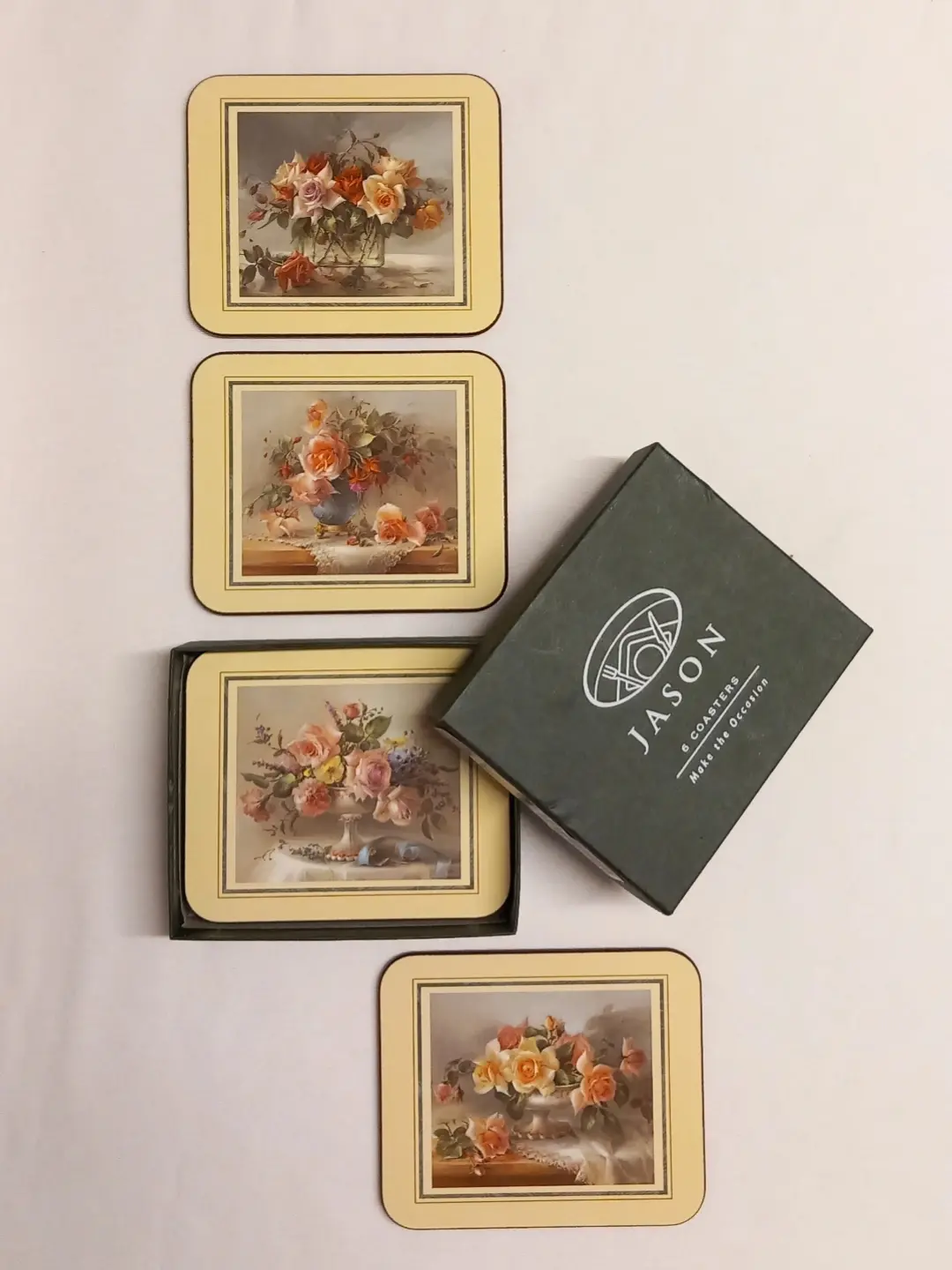 Dört gül natürmortlu bardak altlığı ve yeşil JASON 6 Coasters kutusunun üstten görünümü