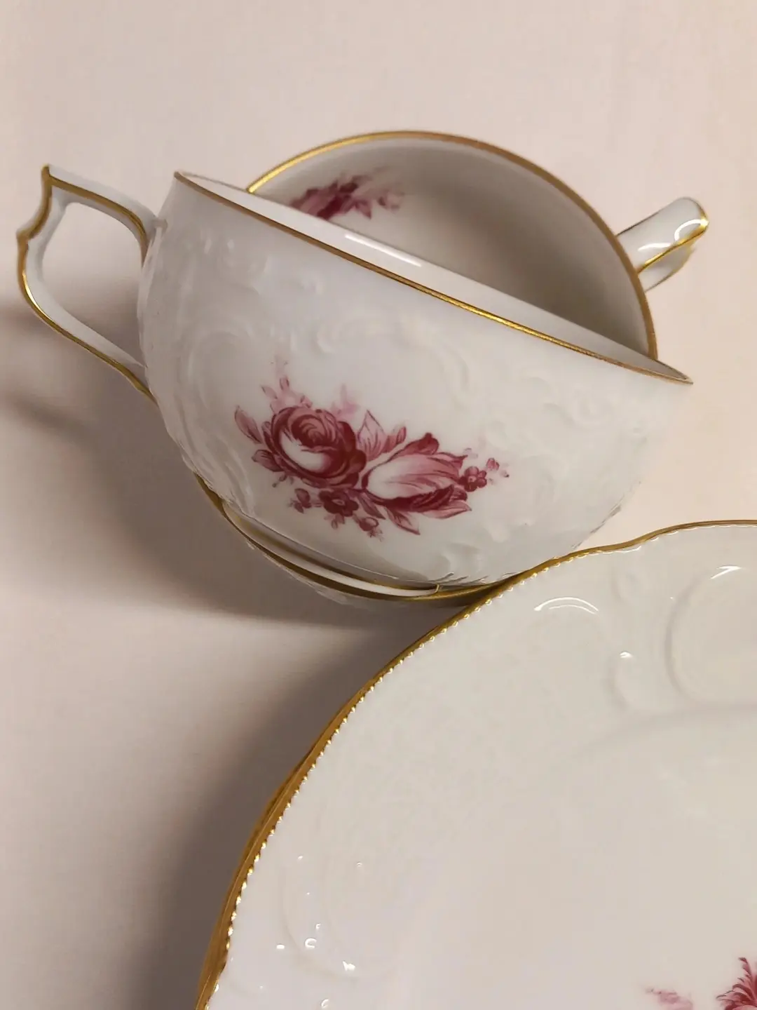 Rölyefli beyaz porselen, gül kurusu çiçekli ve altın yaldızlı iki Rosenthal fincan ile tabak kenarı