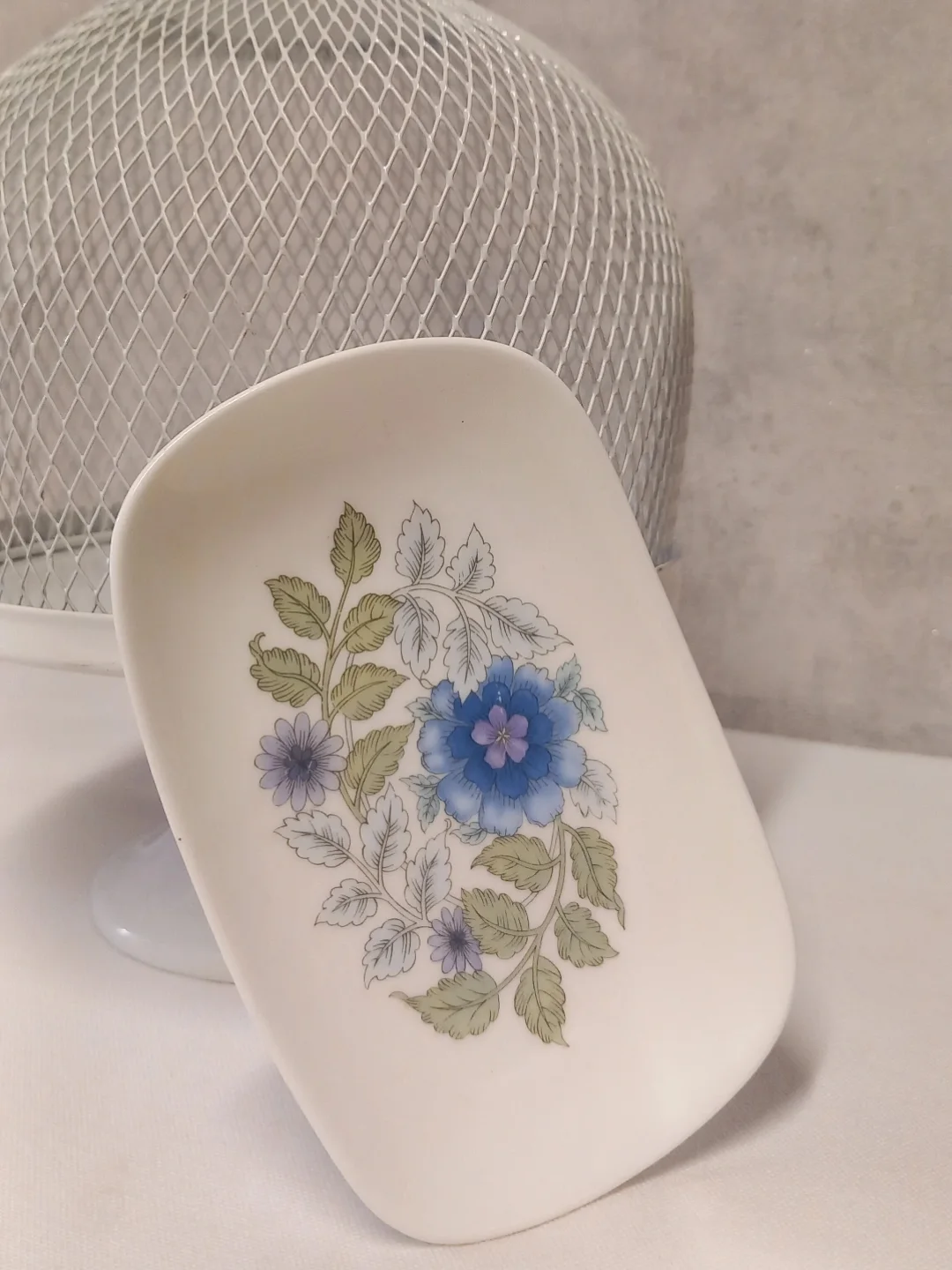 Beyaz tel kafes kubbeye yaslanmış, mavi çiçek ve yeşil yapraklı dikdörtgen Wedgwood porselen sabunluk