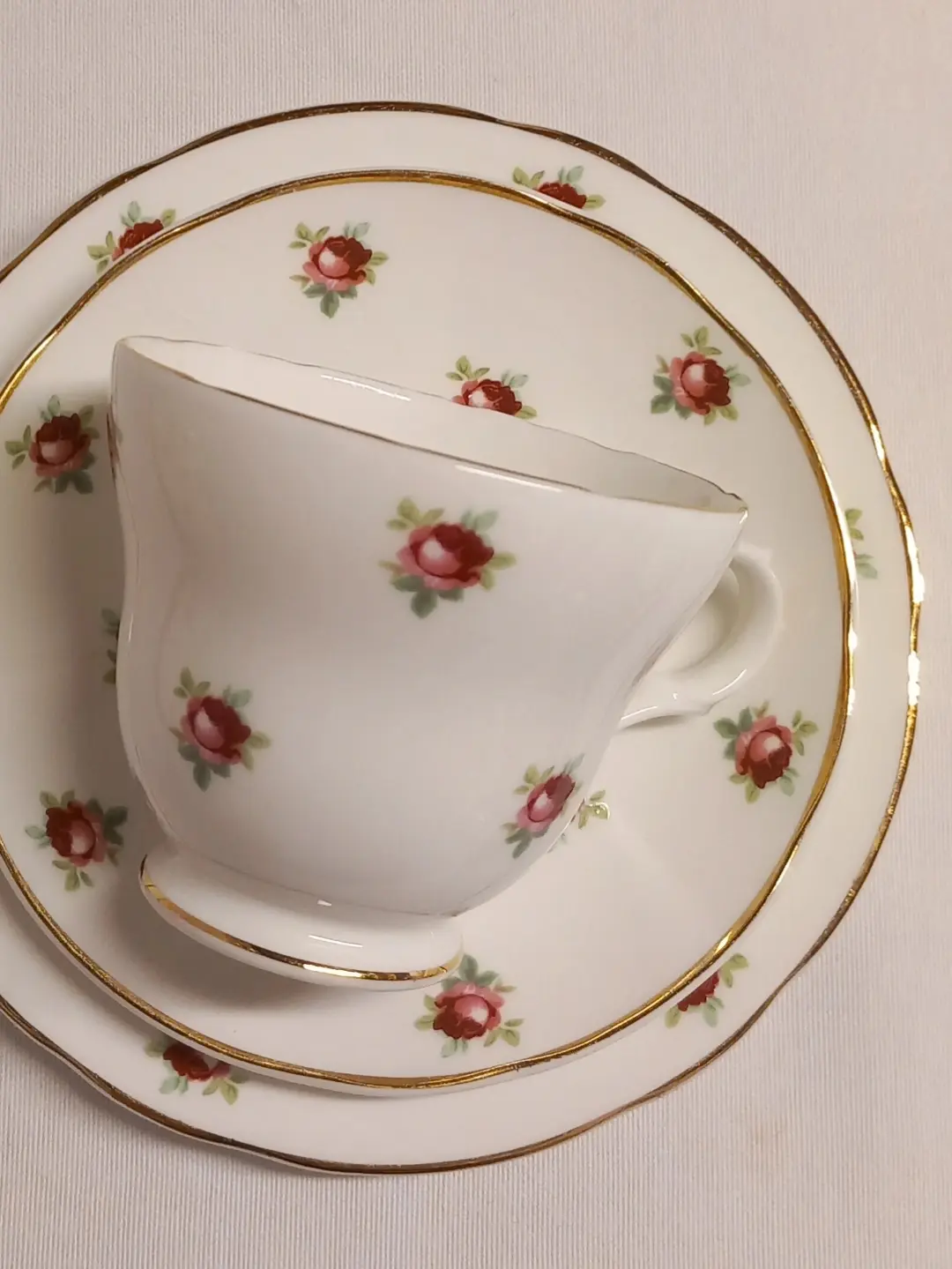 Pembe gül desenli, altın kenarlı çay fincanının fincan tabağı ve pasta tabağıyla üstten görünümü